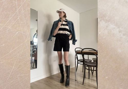 Byrdie writer wears tailored shorts with boots, striped shirt, denim jacket, and cap